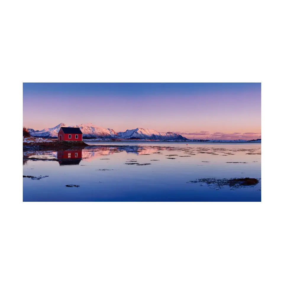 Beautiful winter lake, red rorbu house and snowy mountains at sunset